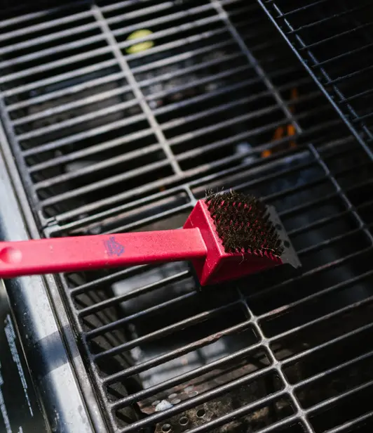 A red grill brush sitting on top of an outdoor grill.