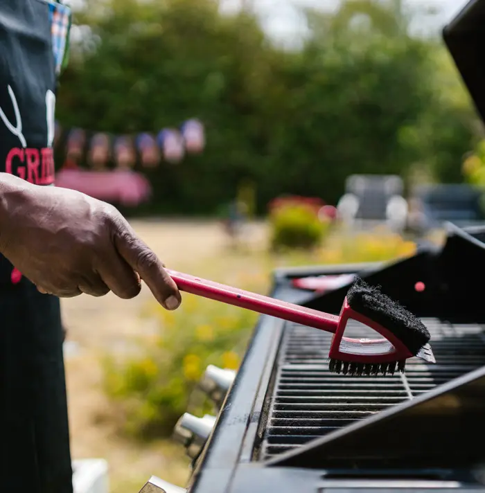 A person is using the grill brush to clean the grill.