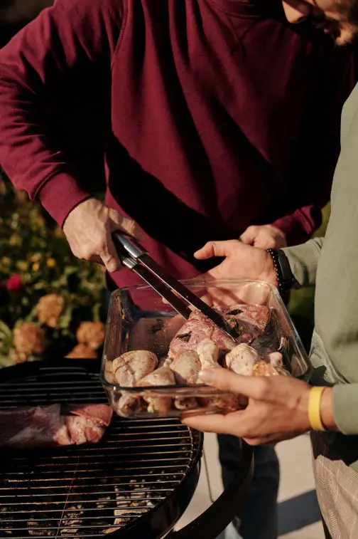 A person holding a tray of food on top of a grill.