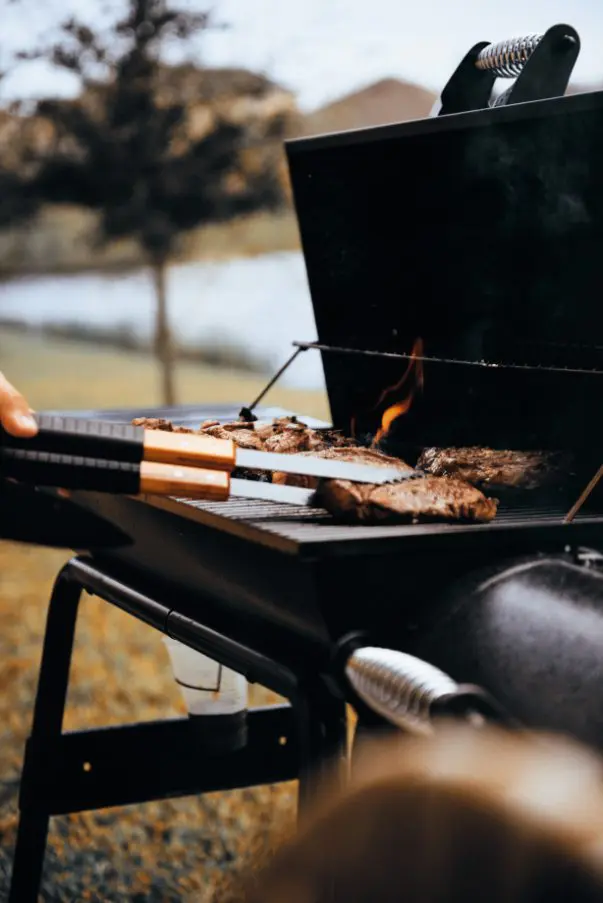 A person is cooking meat on an outdoor grill.