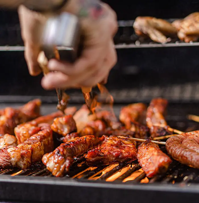 A person grilling meat on top of an open grill.